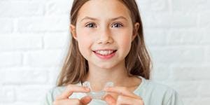 A smiling child holds Invisalign clear aligners