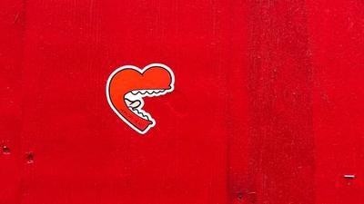 A heart shaped mouth with white teeth and long tongue, graffiti on a red wall
