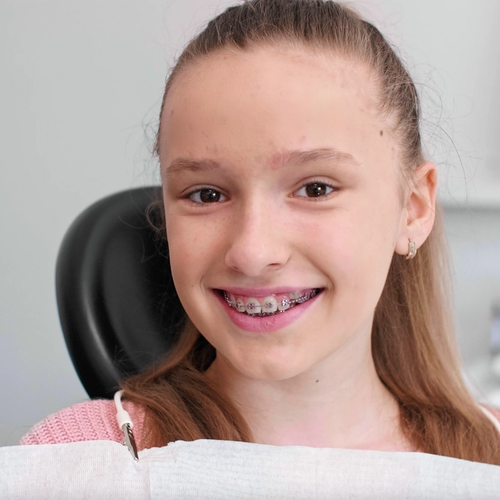 A young girl with fixed braces sits in a dental chair, portrait.