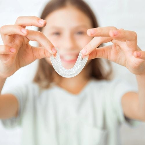 A child holds clear aligners to the camera, reminiscent of a smile