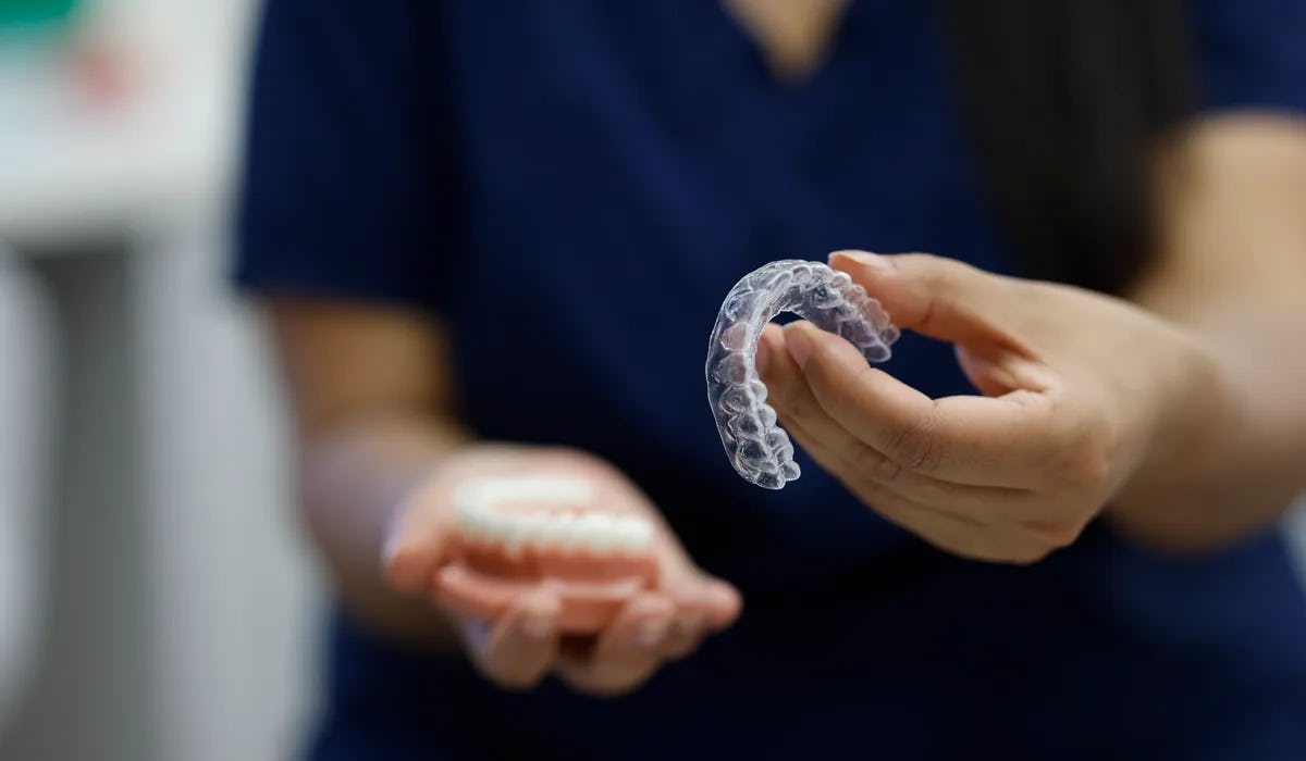 An orthodontist in soft focus holds up clear aligners to the camera