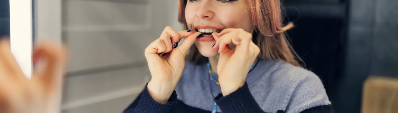 A teenager inserts Invisalign Teen clear aligners while looking in the mirror