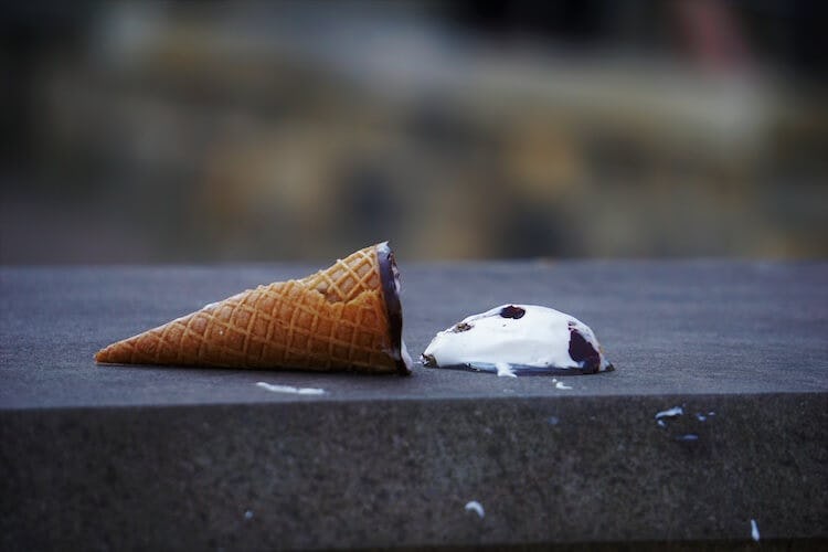 An ice cream cone dropped on the floor. The ice cream is melting sadly.