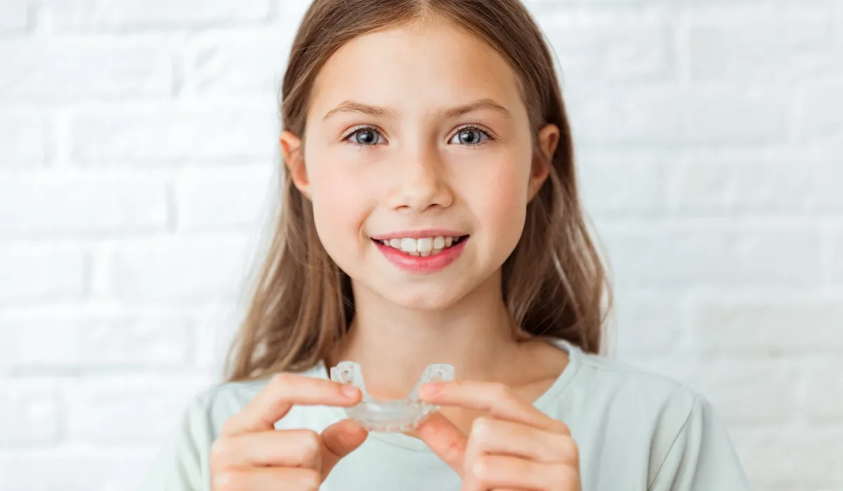 A smiling child holds Invisalign clear aligners