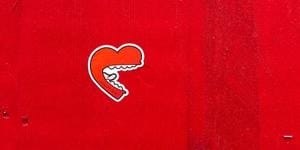 A heart shaped mouth with white teeth and long tongue, graffiti on a red wall