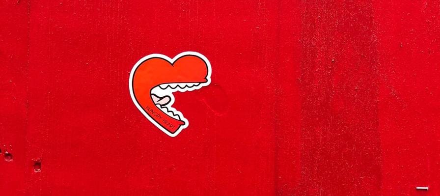 A heart shaped mouth with white teeth and long tongue, graffiti on a red wall