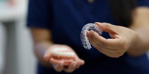 An orthodontist in soft focus holds up clear aligners to the camera