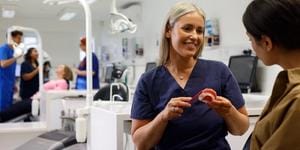 A close up on an orthodontist inspecting a mouth with fixed braces and colourful bracket modules