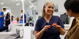 A close up on an orthodontist inspecting a mouth with fixed braces and colourful bracket modules