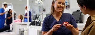 A close up on an orthodontist inspecting a mouth with fixed braces and colourful bracket modules