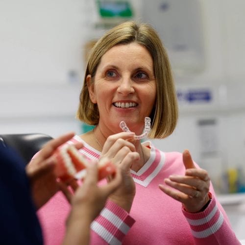 A close up on a hand holsing Invisalign aligners on a a pastel pink background